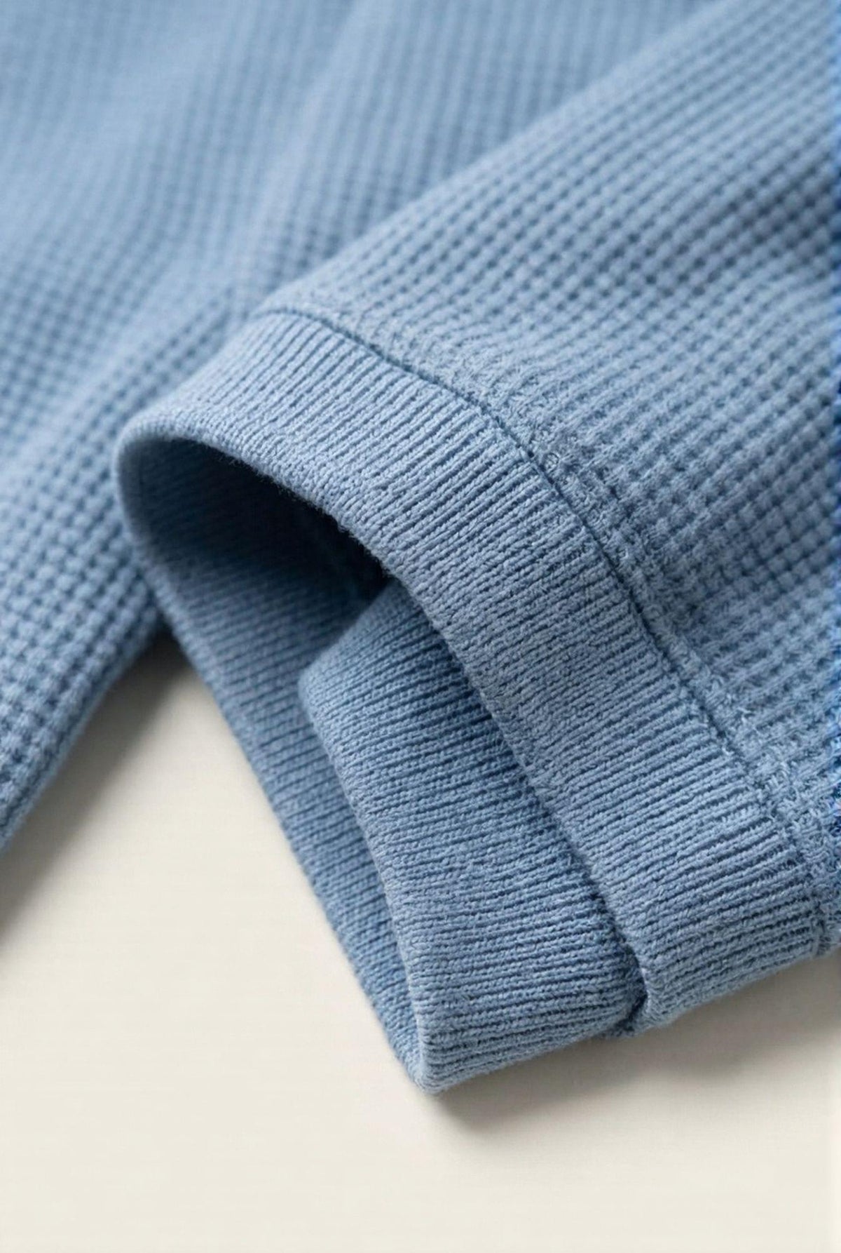Close-up of blue waffle knit men's sweater sleeve, showcasing soft texture and ribbed cuff detail
