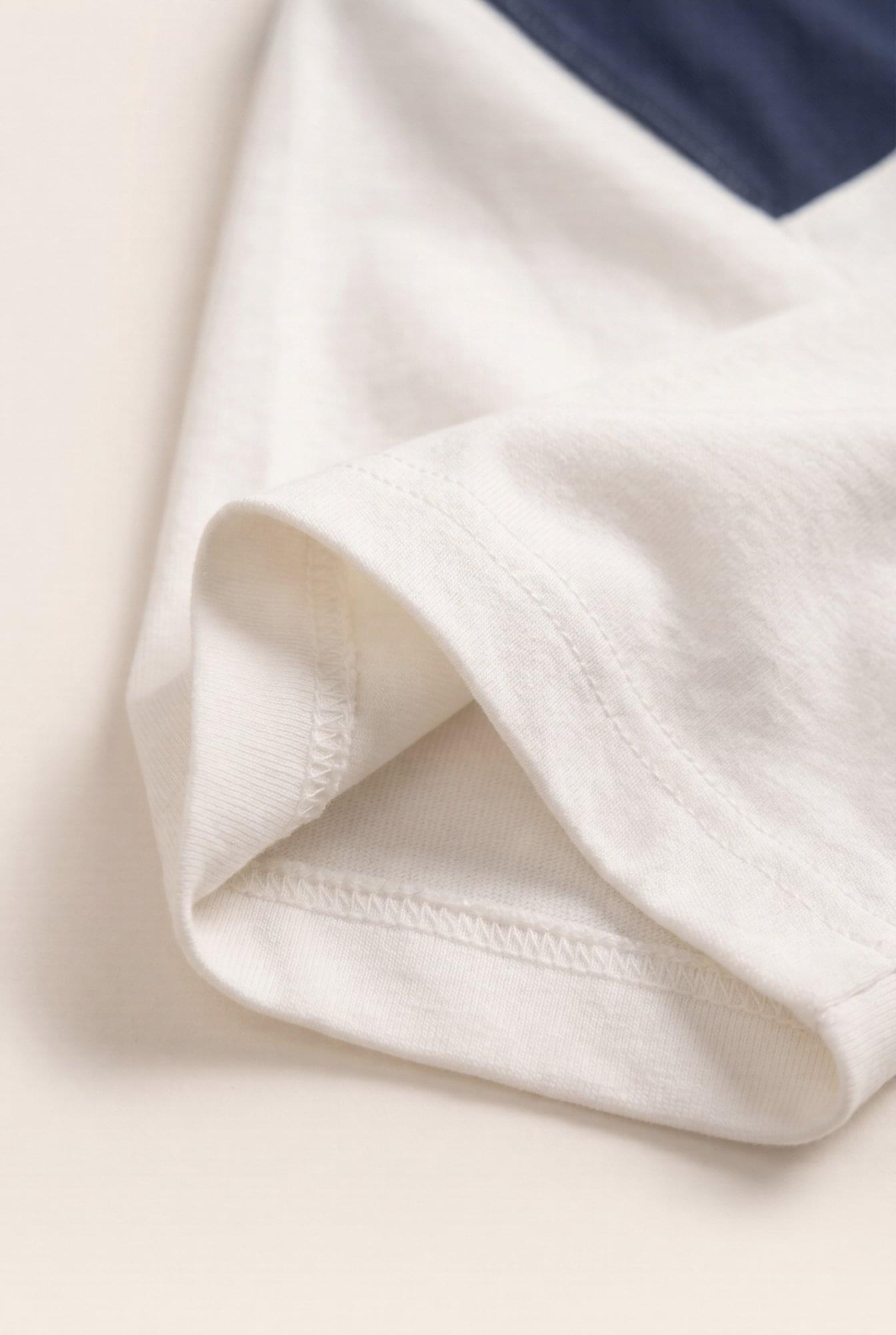Close-up of premium white men's t-shirt sleeve with neat stitching and navy detail, showcasing quality fabric and modern style.