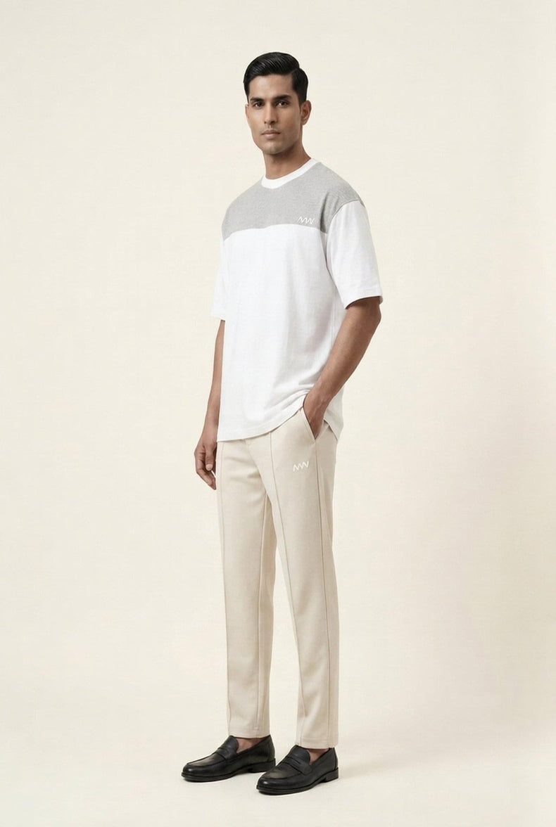 Man wearing modern men's clothing: white and gray color-block t-shirt with beige pants and black loafers
